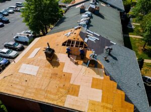 A roofer in safety gear examines shingles on a sloped suburban house roof during daylight.